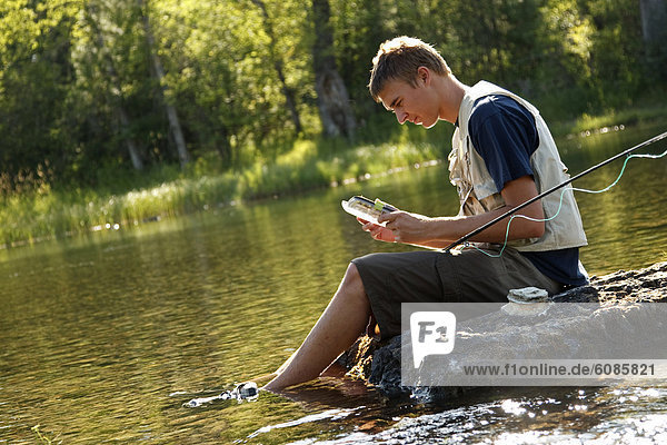 A teenage boy sits on a rock as he chooses a fly while fly fishing on the Swan River near Bigfork  Montana.