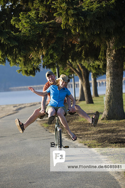 A young woman rides on the handle bars of a young man's cruiser bike in Sandpoint  Idaho.