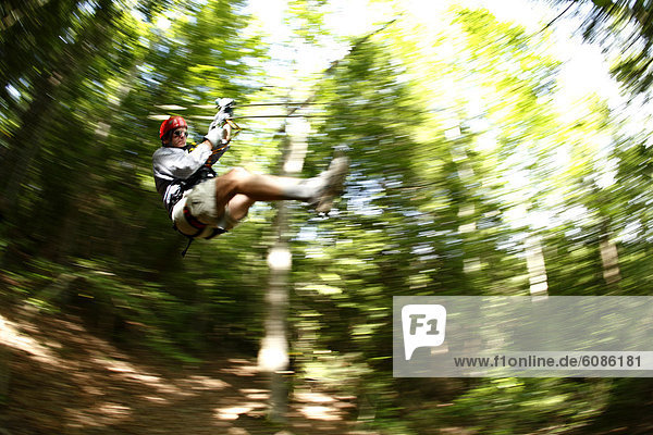 Pan-blur image of man on a zip-line in the tree canopy.