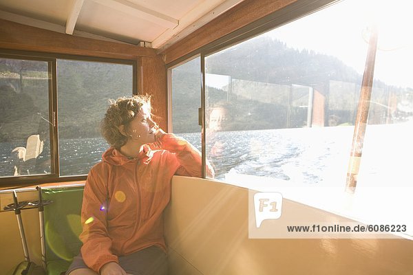 After a long hike a woman takes in sun through window on back of a boat on a lake.