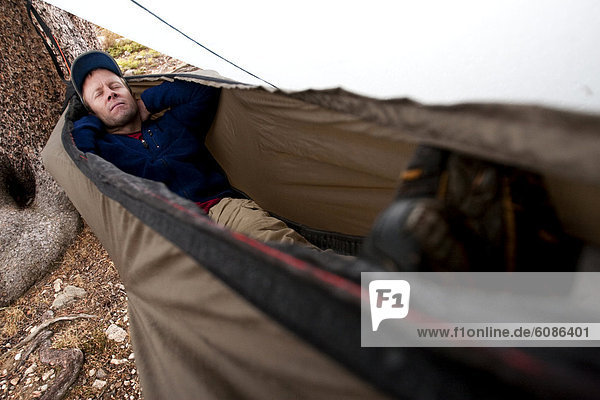 A man takes a short rest in a hammock with a rain fly during rainy weather in the Snowy Range  Wyoming.