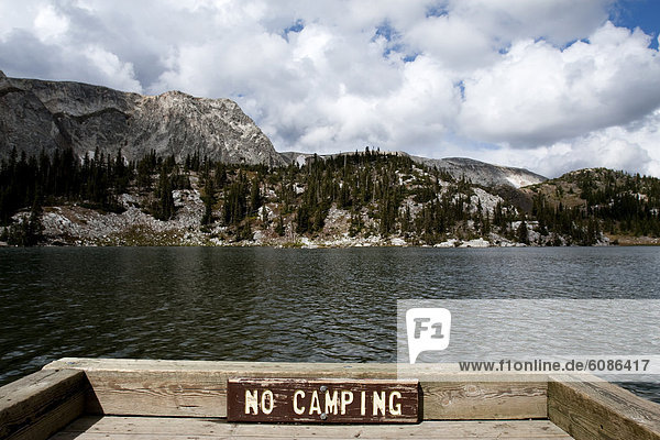 'A sign reading ''No camping'' sits on a fence above an alpine lake  Mirror Lake  in the Snowy Range  Wyoming.'