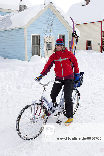 A woman bikes on a snowy street with her skis in winter  Crested Butte  Colorado.