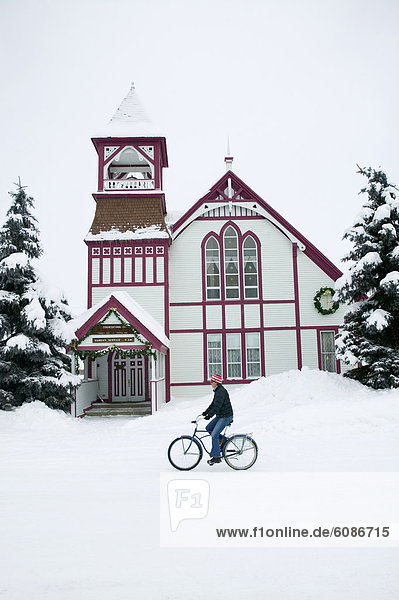 Woman riding a bike down a snow covered road in front of a church  Crested Butte  Colorado.