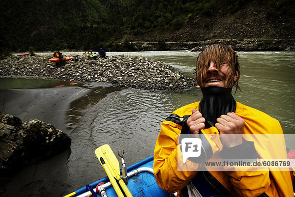 A young male rafter pulls his head through the gasket on his drysuit during a whitewater rafting trip in Western China.
