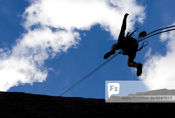 A young man is silhouetted as he rappels down a rock in Bishop  California.