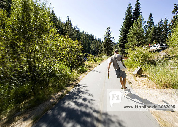 A young man rides a skateboard while carrying a fishing pole in his hand in Truckee  California.
