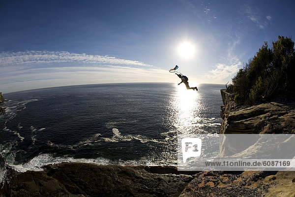 A BASE jumper leaps off a cliff over the ocean in Sydney  New South Wales  Australia.