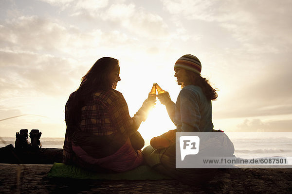 Two beautiful women and toast a beer while enjoying the sunset at La Push Beach  from a drift log.