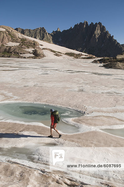 A woman hiking on still-frozen lake in summer  Weminuche Wilderness  San Juan National Forest  Colorado