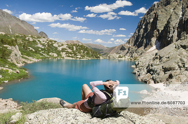 A woman hiker rests next to turquoise lake  Weminuche Wilderness  Colorado.