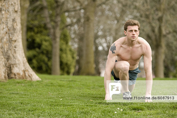 An athletic male stretches in a park before running.