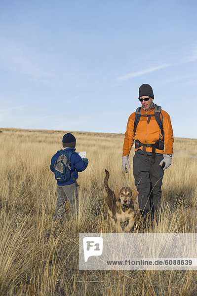 A young boy reads a map on a hike with his dad and dog.