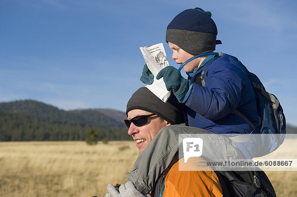 A young boy catches a ride on his dad's shoulders while reading a map.