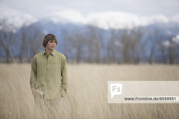 A young man enjoys a winter stroll through a field of grass with mountains in the background.