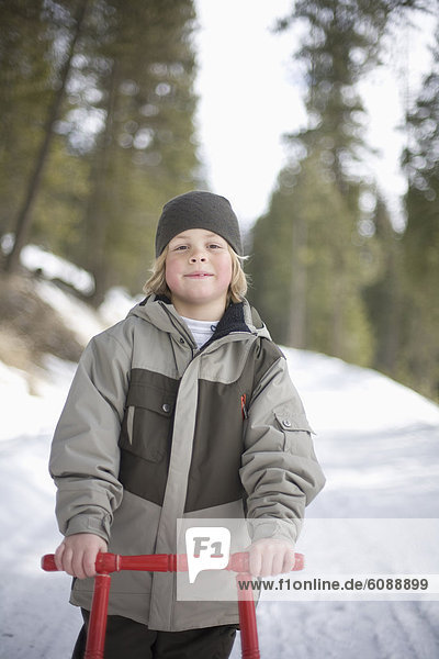 A portrait of a young boy and his sled outside on a snowy road.