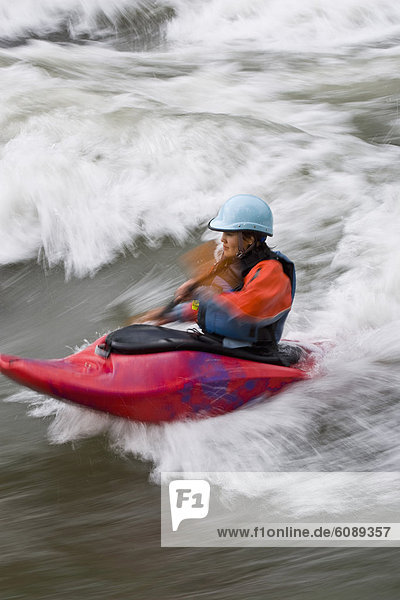 A young  Asian-looking woman surfing a wave in a whitewater kayak  Elk river  East Kootenies  British Columbia  Canada.