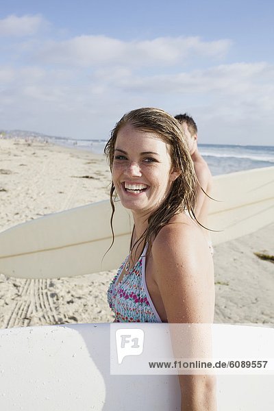 Young female surfer walks out of the water holding her surf board  looks at the camera and smiles at Pacific Beach  San Diego  California.