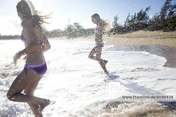 Two pre-teen girls running to the water at Paia Beach  Maui  Hawaii smile as they get wet.