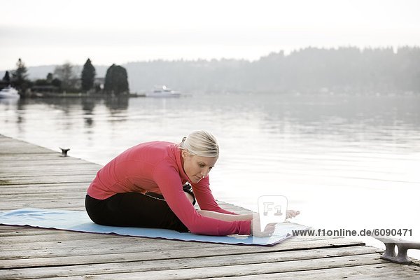 A young woman hanging out on a dock over Lake Washington while stretching on a yoga mat.