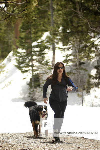 A female running with her dog in the mountains.