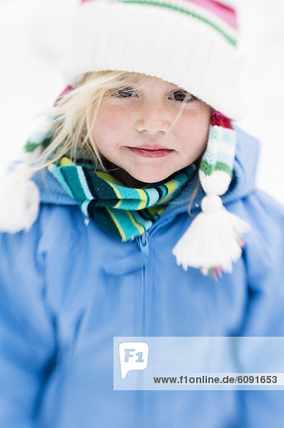 Young girl smilies with pink cheeks in the winter snow with select focus.