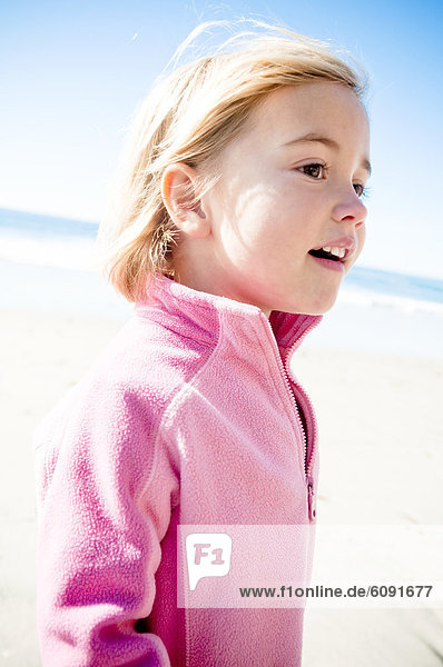 A young girl smiles while walking down the beach.