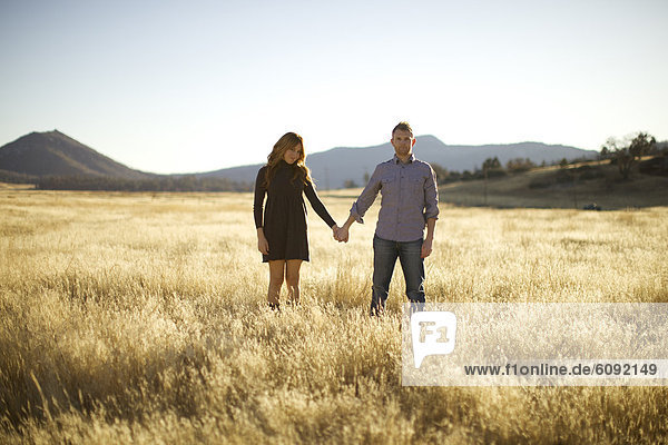 Couple hold hands  look as the camera and smile in an open field