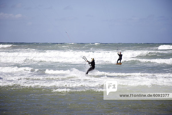 Two male kitesurfers riding together.
