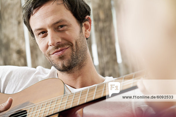 Mittlerer Erwachsener Mann zupft Gitarre  lächelnd  Nahaufnahme