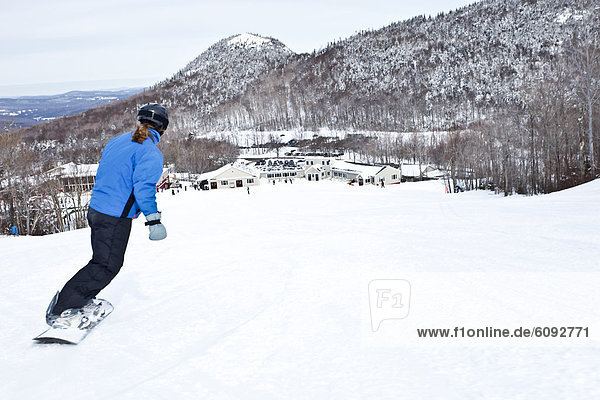 A female snowboarder riding down to the lodge in New Hampshire.