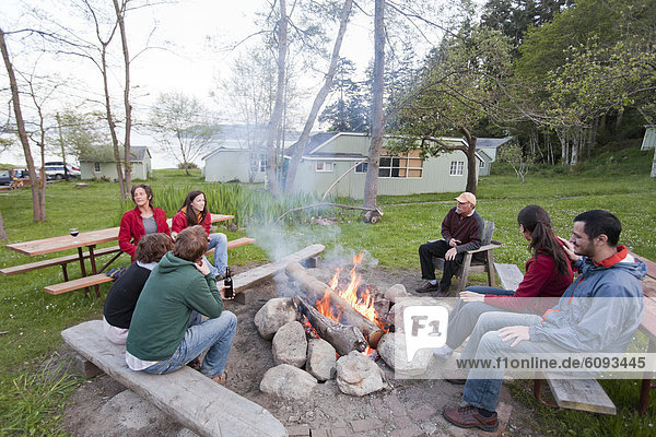 A group of 7 friends sit around a camp fire at a rustic resort.