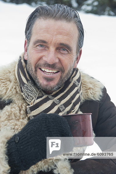 Österreich  Salzburger Land  reifer Mann mit Teetasse im Schnee  lächelnd  Portrait