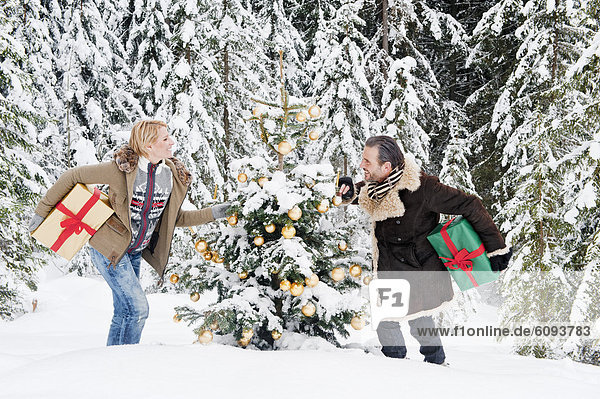 Österreich  Salzburger Land  Paar hält Weihnachtsgeschenk im Schnee  lächelnd