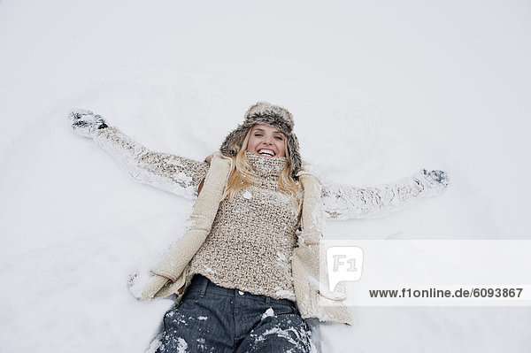 Österreich  Salzburger Land  Mittlere erwachsene Frau auf Schnee liegend  lächelnd