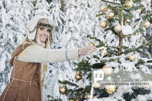 Österreich  Salzburger Land  Mittlere erwachsene Frau  Kerze am Weihnachtsbaum anzünden  lächelnd  Portrait