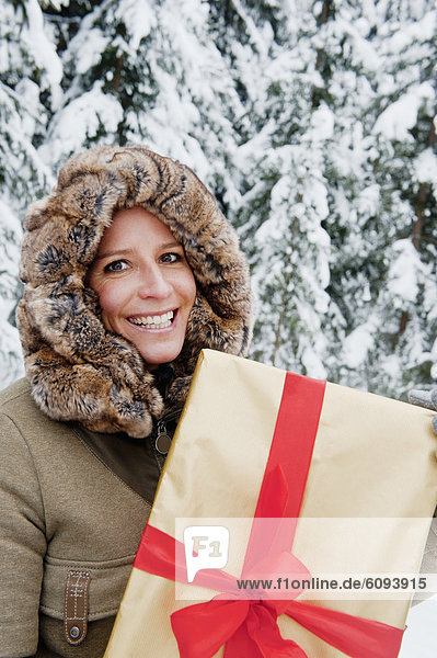 Österreich  Salzburger Land  Mittlere erwachsene Frau stehend mit Weihnachtspäckchen  lächelnd  Portrait