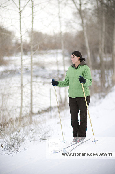 Woman cross country skiing next to river.