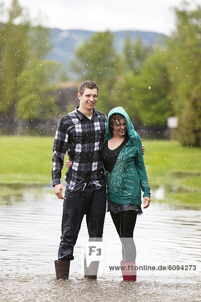 A young couple stands in a large puddle after having a water fight.