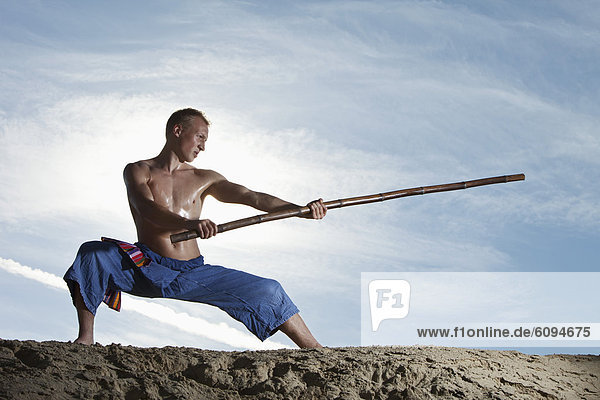 Young man doing martial arts training with stick