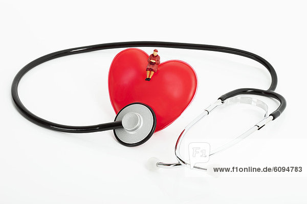 Figurine sitting on heart with stethoscope on white background