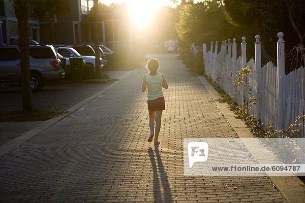 A young girl is walking down an alley into the sun.