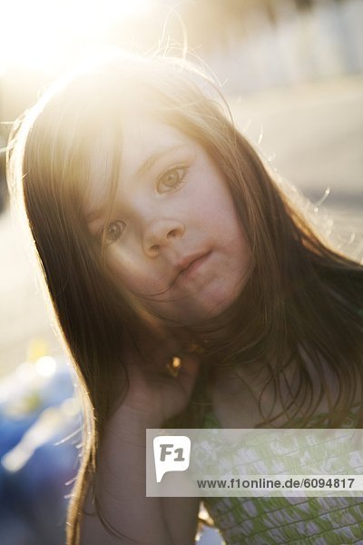 A little girl with long hair is staring at the camera with the sun shining through her hair.