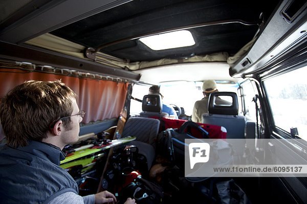Three men riding in a classic van with ski equipment everywhere.