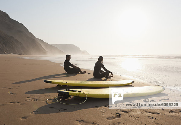 Portugal  Paar sitzend am Strand mit Surfbrett