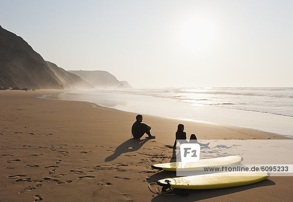 Portugal  Paar sitzend am Strand mit Surfbrett