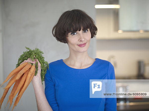 Young woman with carrots in kitchen  smiling  portrait