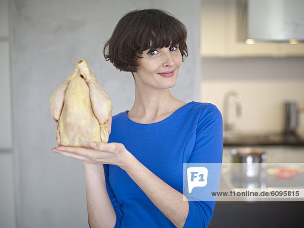 Young woman with raw chicken in kitchen  smiling  portrait