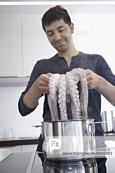 Mid adult man cooking octopus in kitchen  smiling