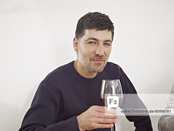 Mittlerer erwachsener Mann trinkt Wein in der Küche  lächelnd